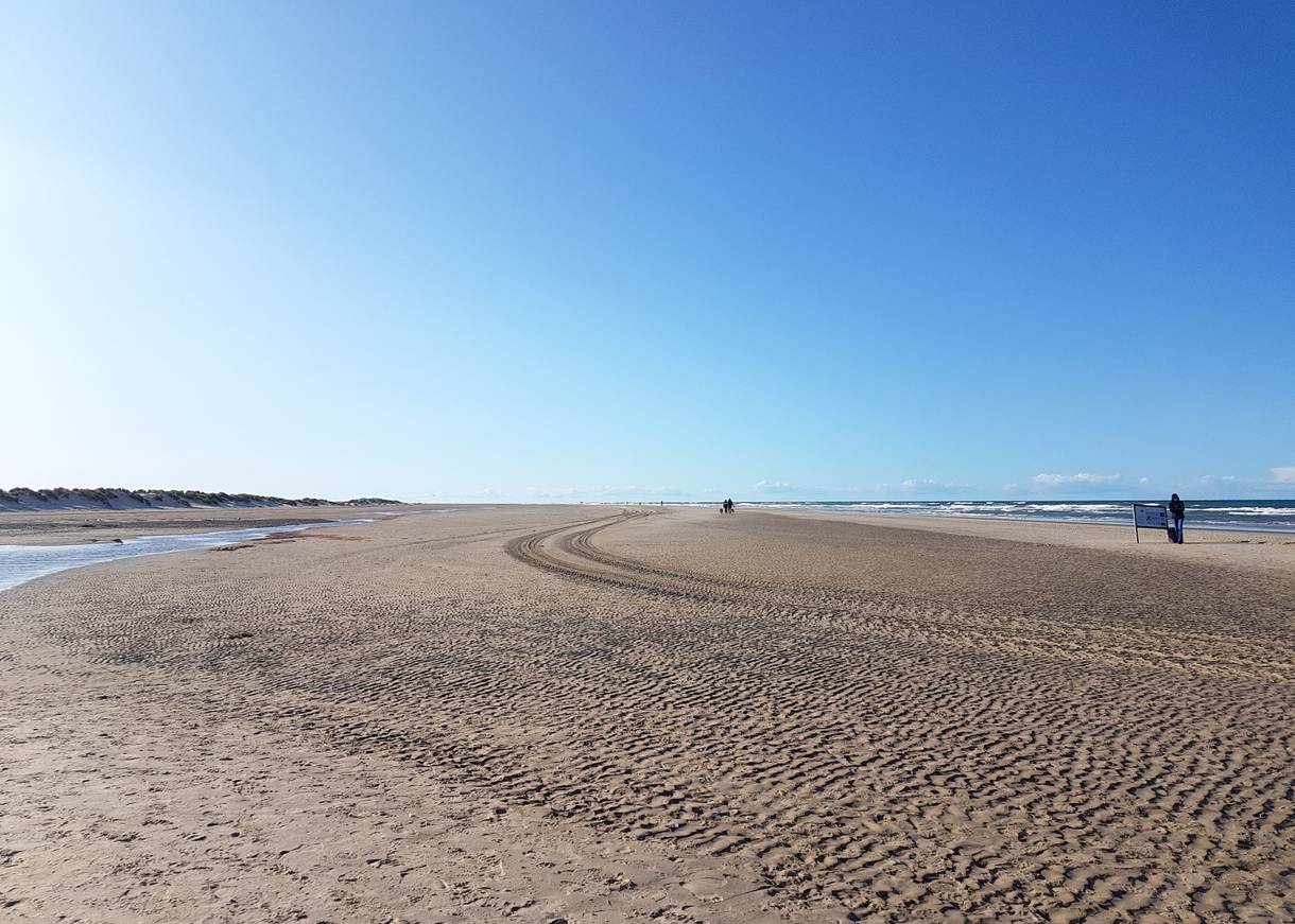 Breiter Strand mit Treckerspuren und vereinzelten Spaziergängern