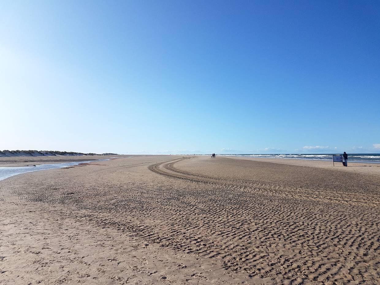 Breiter Strand mit Treckerspuren und vereinzelten Spaziergängern