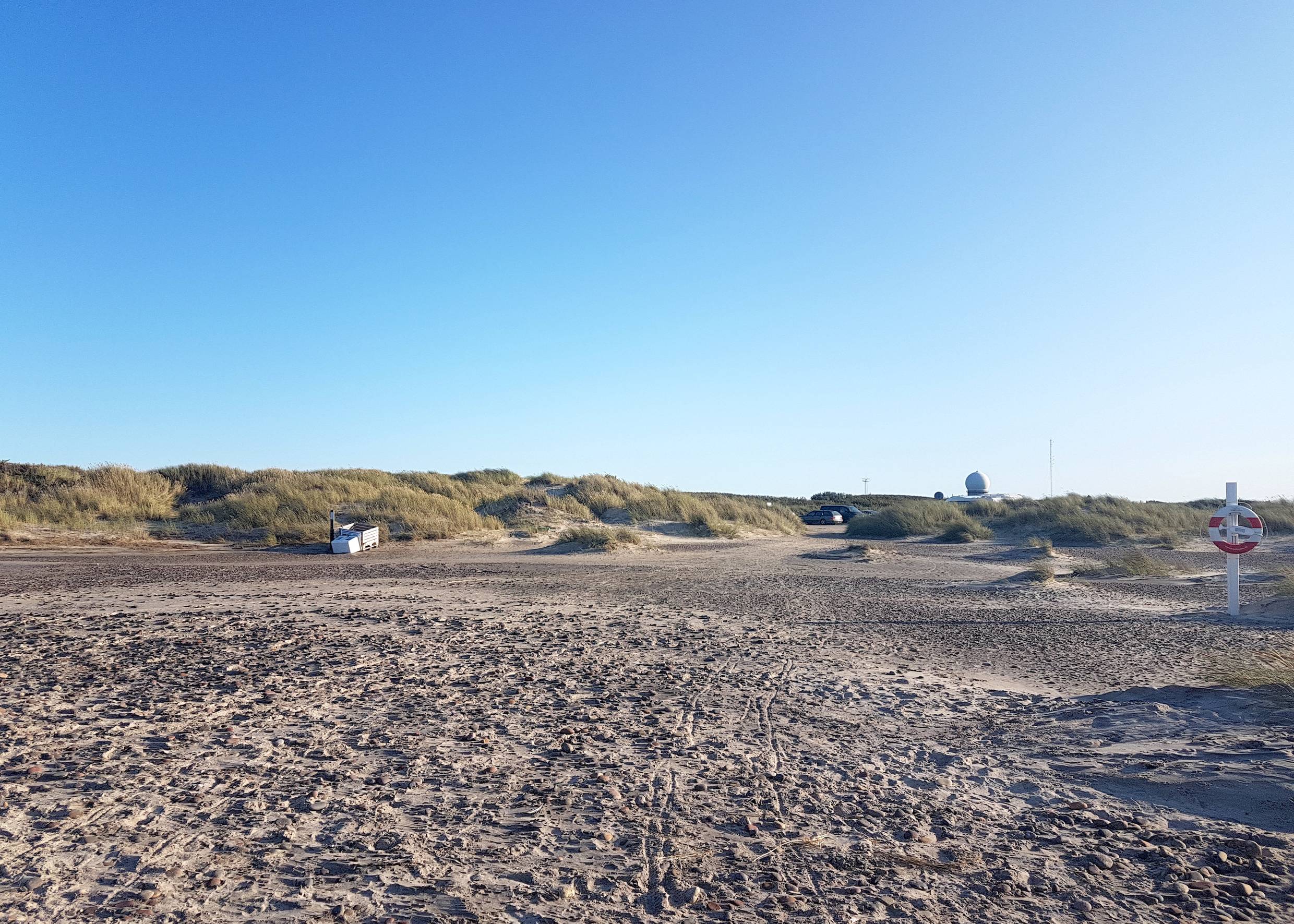 Strandzugang vom Meer aus gesehen, hinter den Dünen eine weiße Kugel, daneben Antennen