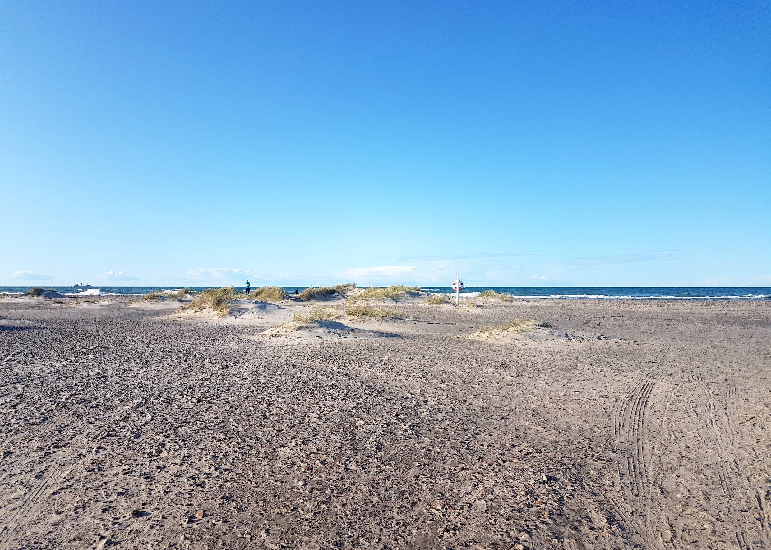Blick auf einen steinigen Strand mit einem Rettungsring und kleinen Sandhügeln