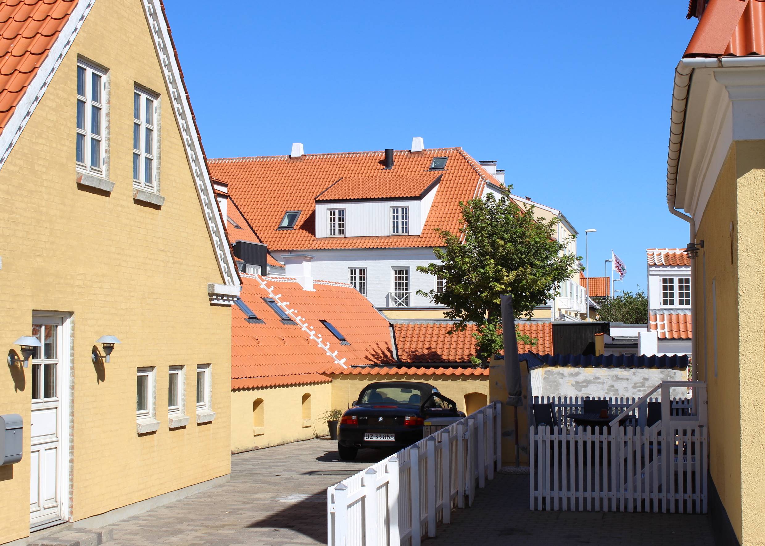 Gelb-weiße Häuser mit rotem Ziegeldach, davor ein weißer Gartenzaun