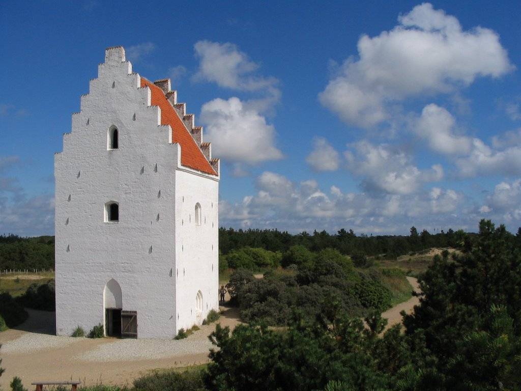 Weißer Kirchturm im Wald, der von Sand umgeben ist
