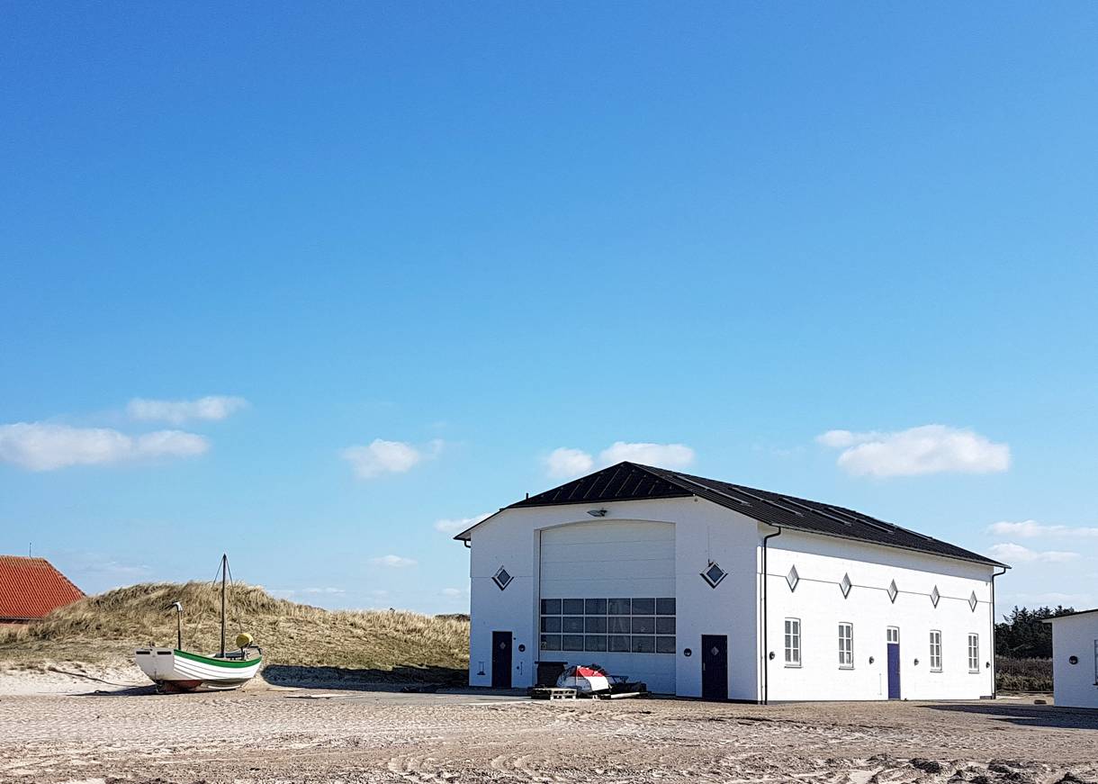Weißes Fischerboot vor einer weißen Halle am Strand