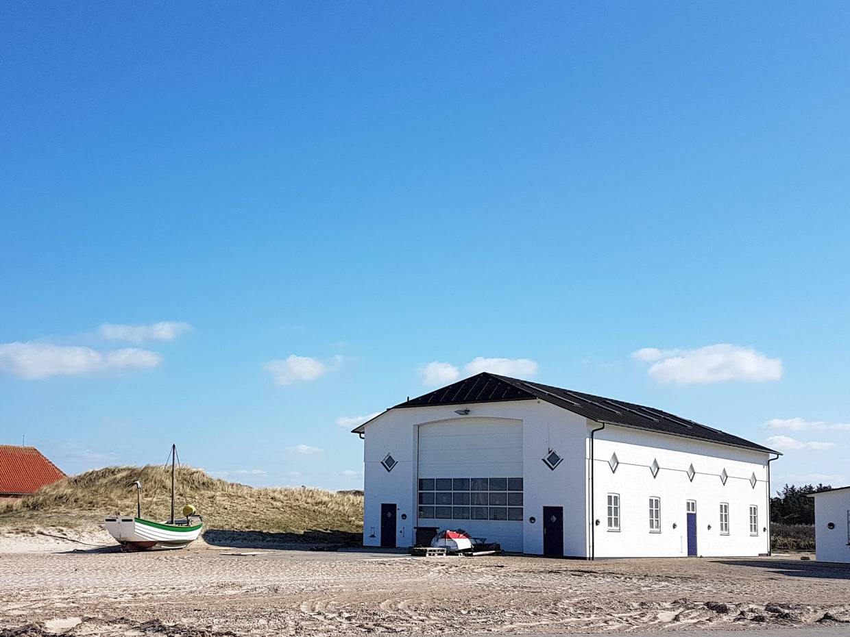 Weißes Fischerboot vor einer weißen Halle am Strand