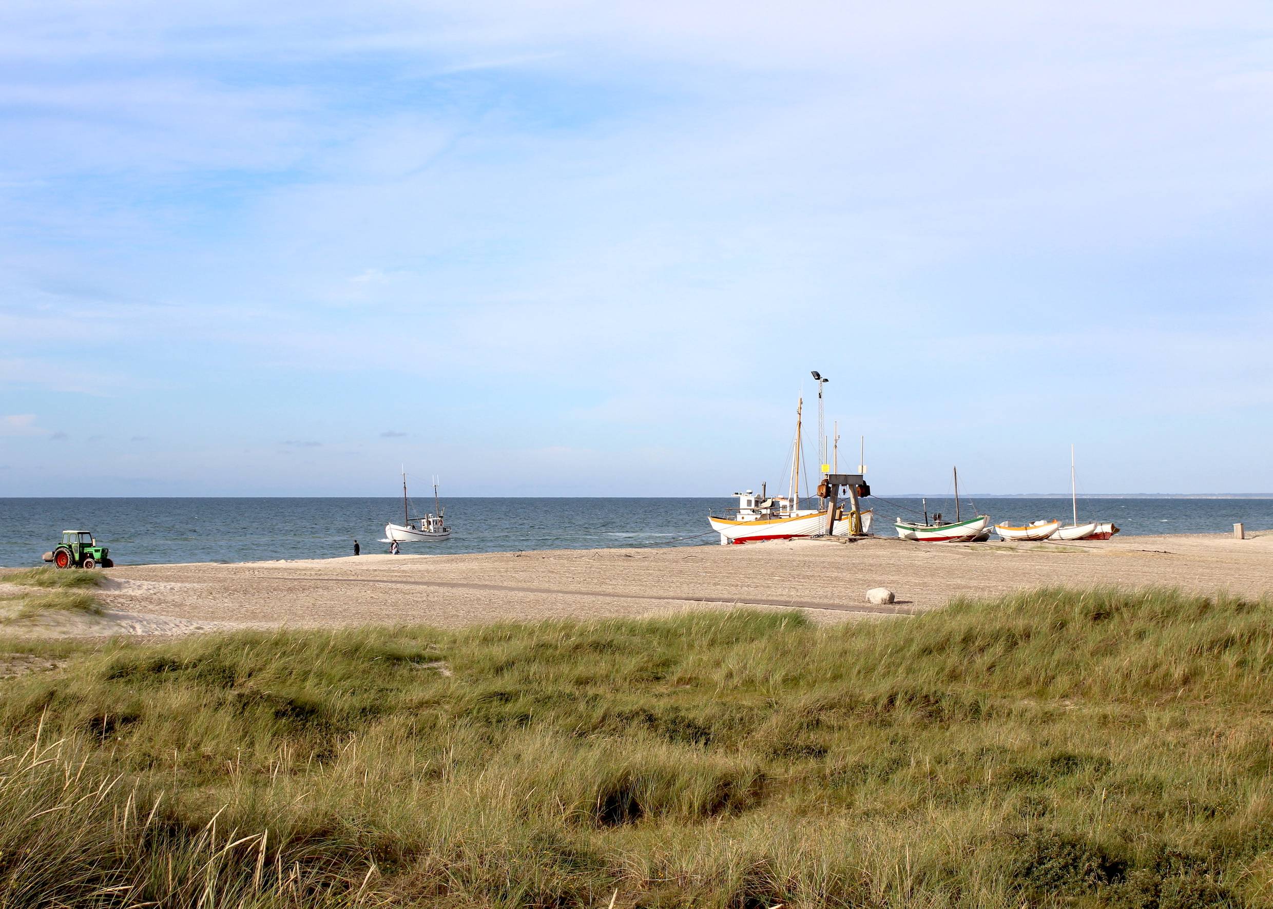 Blick auf weiße Fischerboote und einen Traktor am Strand