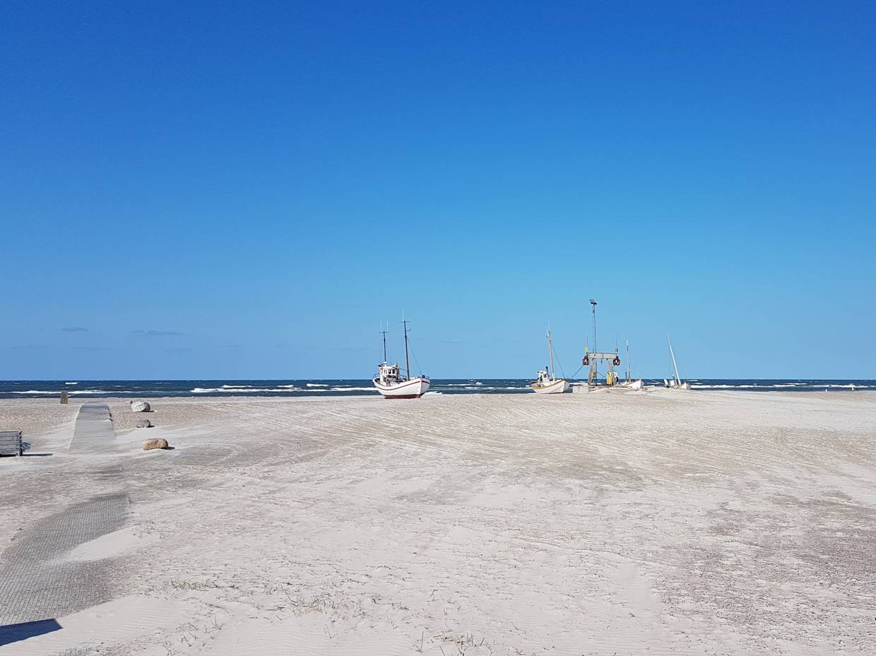 Blick vom Parkplatz auf einen breiten Strand mit zwei Booten auf dem Sand