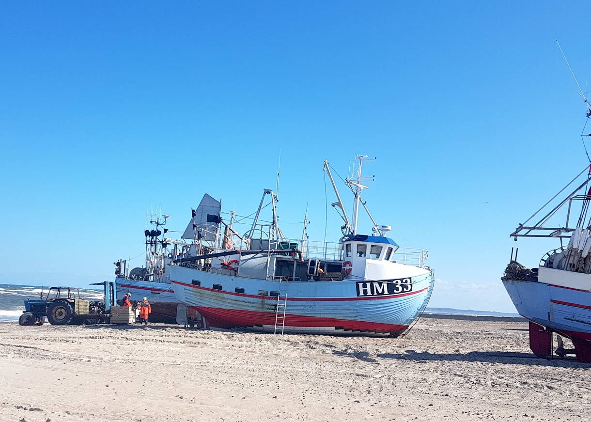 Boote auf dem Strand, davor ein Traktor und Fischer beim Entladen