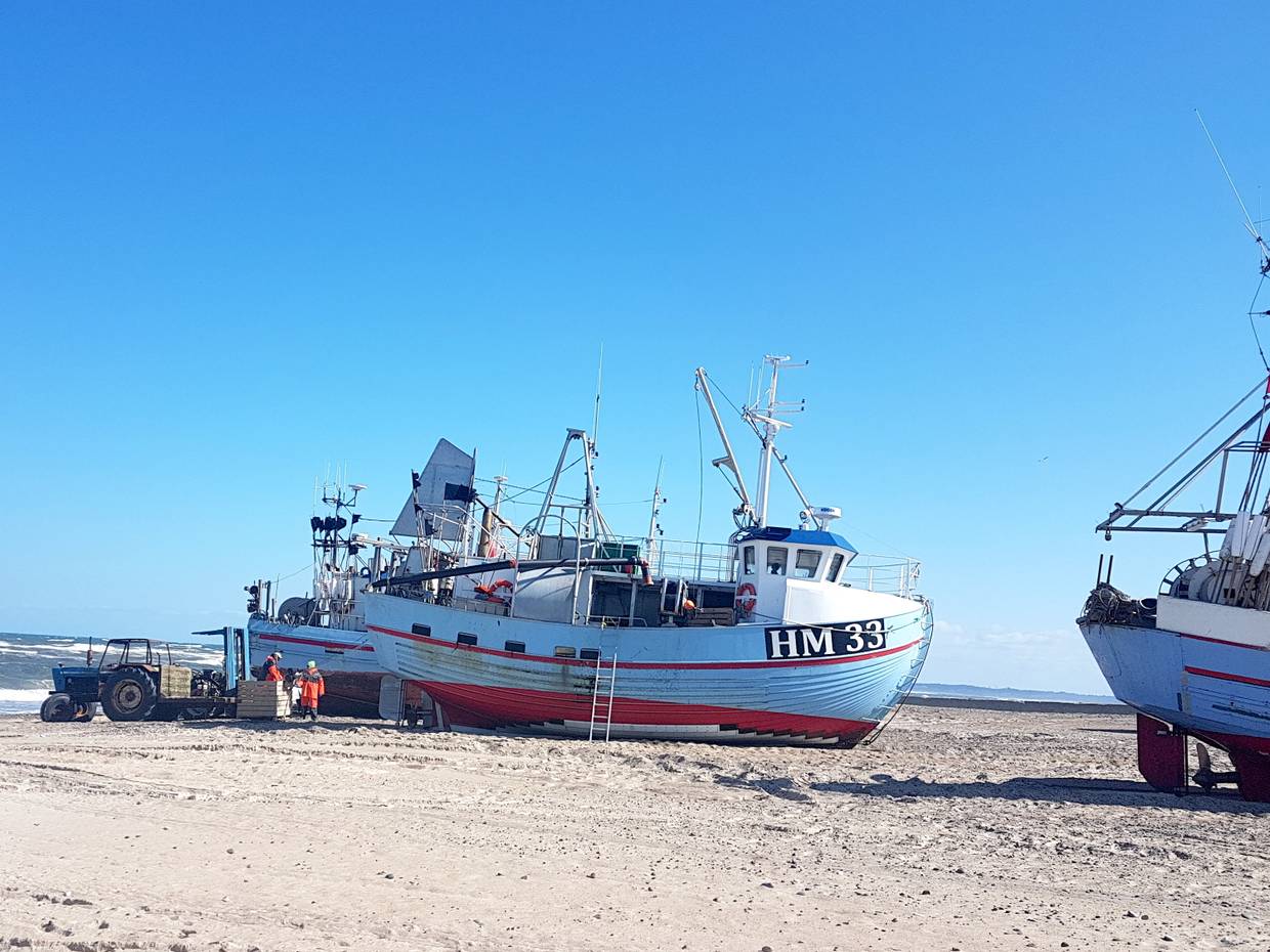 Boote auf dem Strand, davor ein Traktor und Fischer beim Entladen