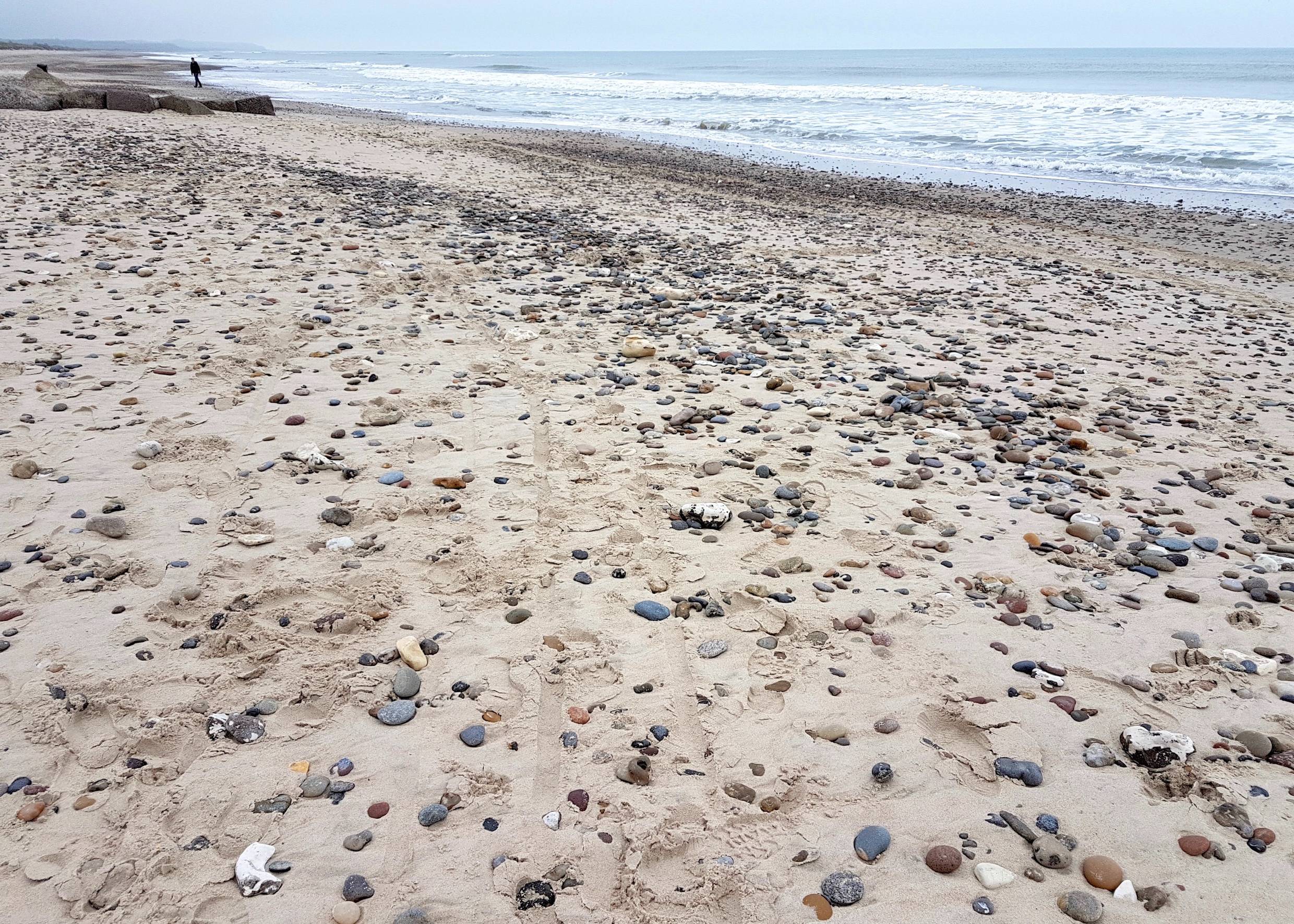 Von kleinen Steinen bedeckter Sandstrand am Meer