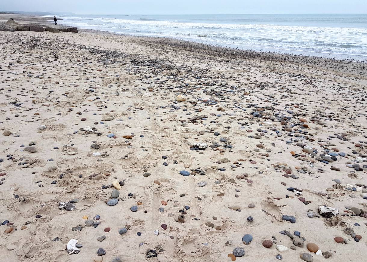 Von kleinen Steinen bedeckter Sandstrand am Meer