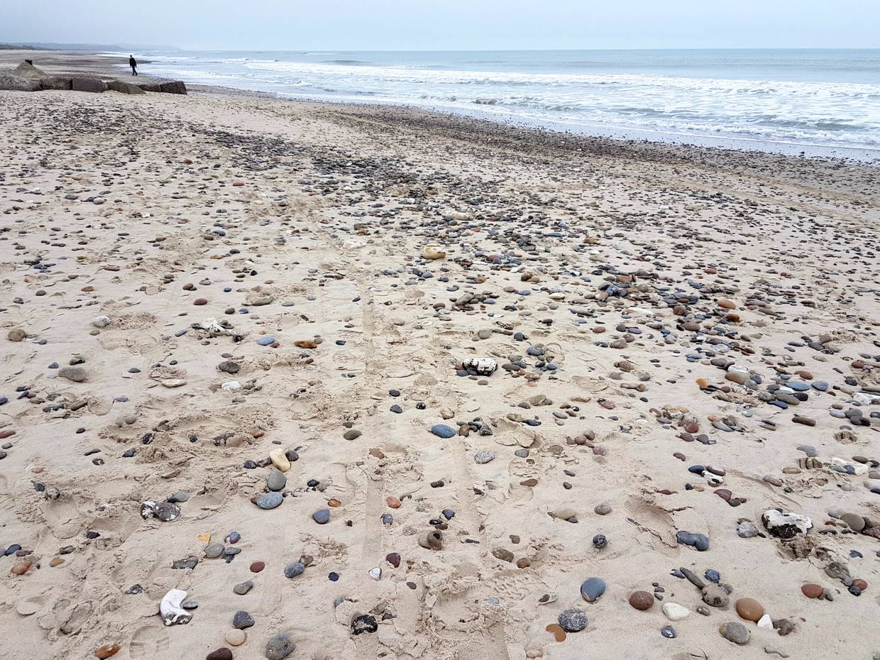 Von kleinen Steinen bedeckter Sandstrand am Meer