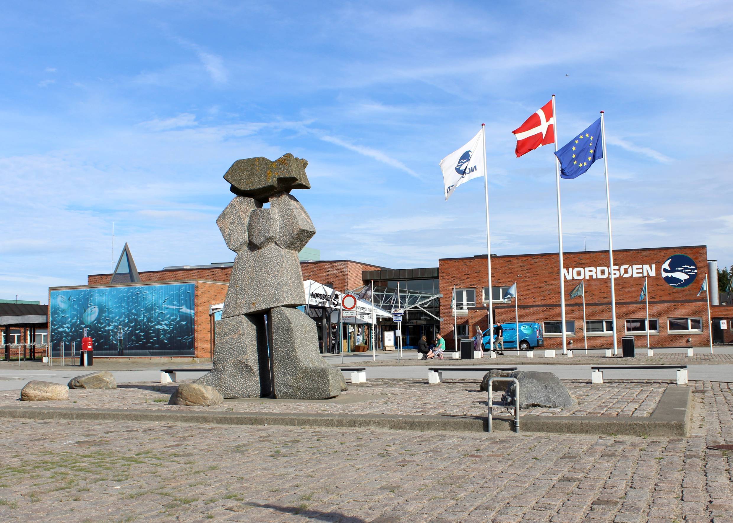 Der Vorplatz zum Aquarium mit drei Fahnenmasten und einer Steinplastik