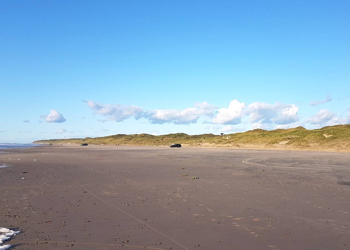 Blick über den Strand in der Abendsonne, im Hintergrund Dünen