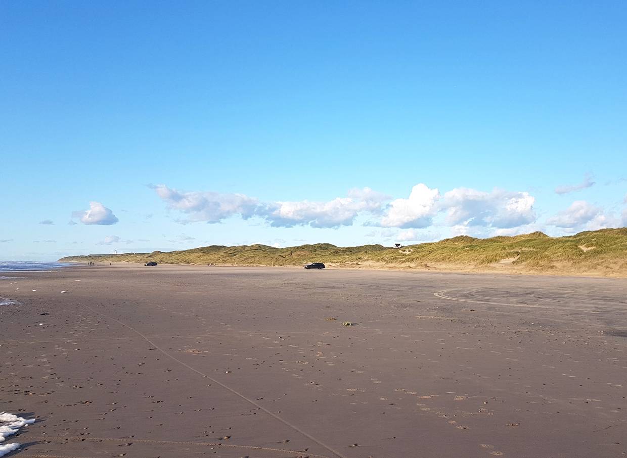 Blick über den Strand in der Abendsonne, im Hintergrund Dünen