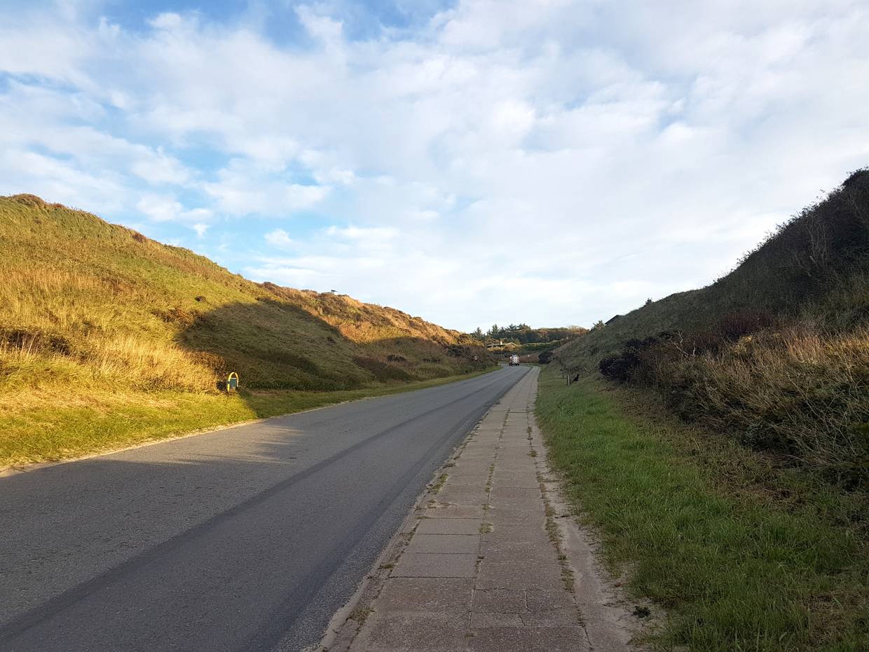 Straße zwischen zwei hohen, grünen Dünen