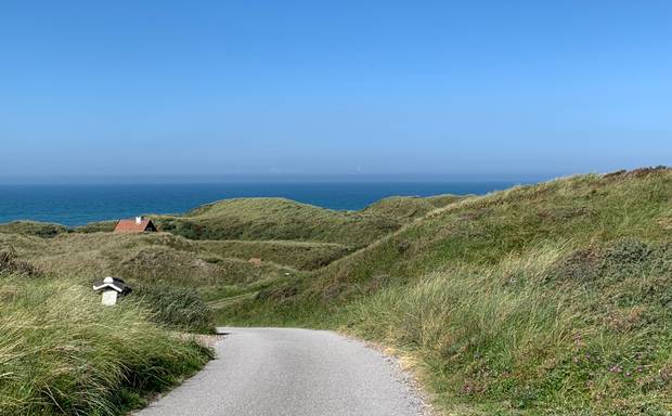 Ein Ferienhaus lässt sich zwischen hohen Dünen erahnen