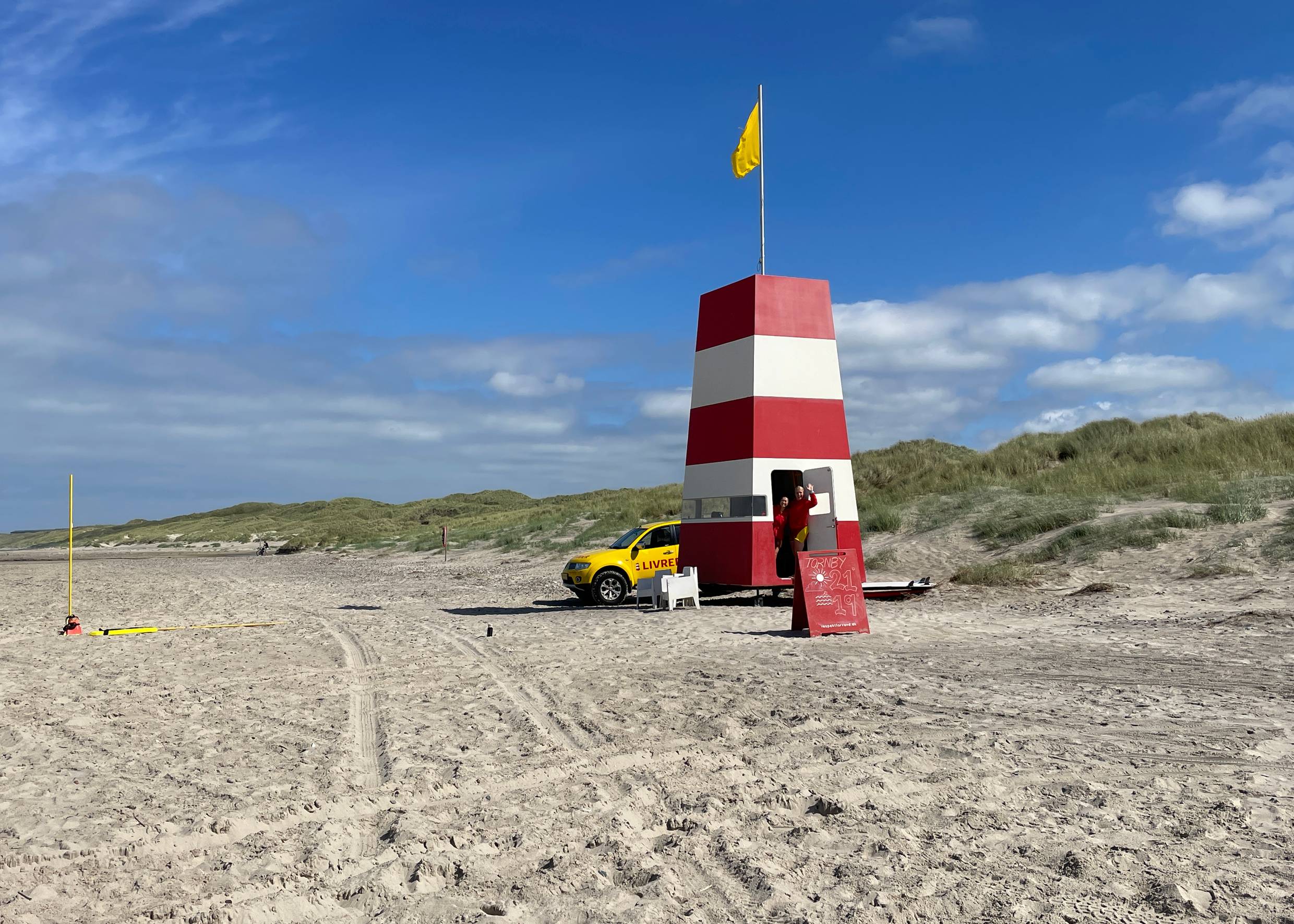 Rettungswacht mit rot-weißem Turm und viele Badegäste mit Autos am Strand