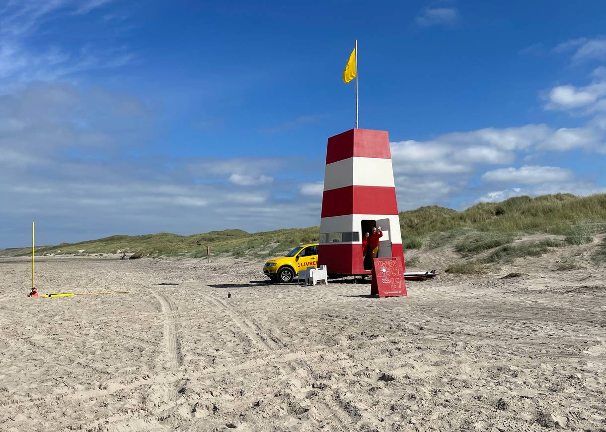 Rettungswacht mit rot-weißem Turm und viele Badegäste mit Autos am Strand