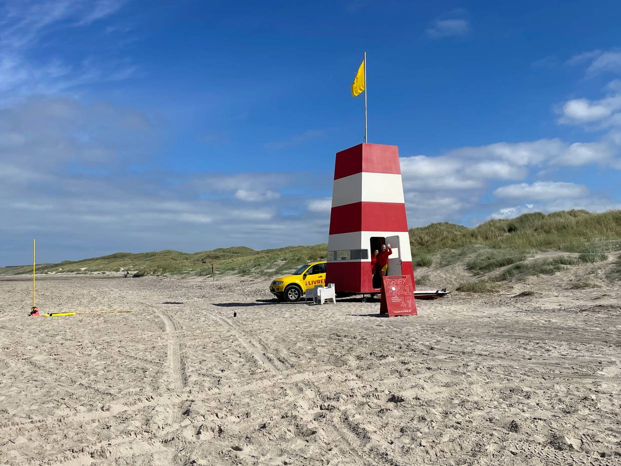Rettungswacht mit rot-weißem Turm und viele Badegäste mit Autos am Strand