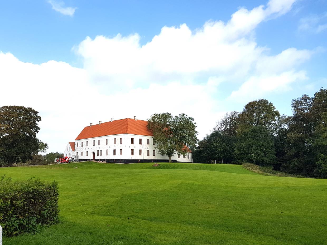 Kleines, weißes Herrenhaus, umgeben von sattgrünem Rasen