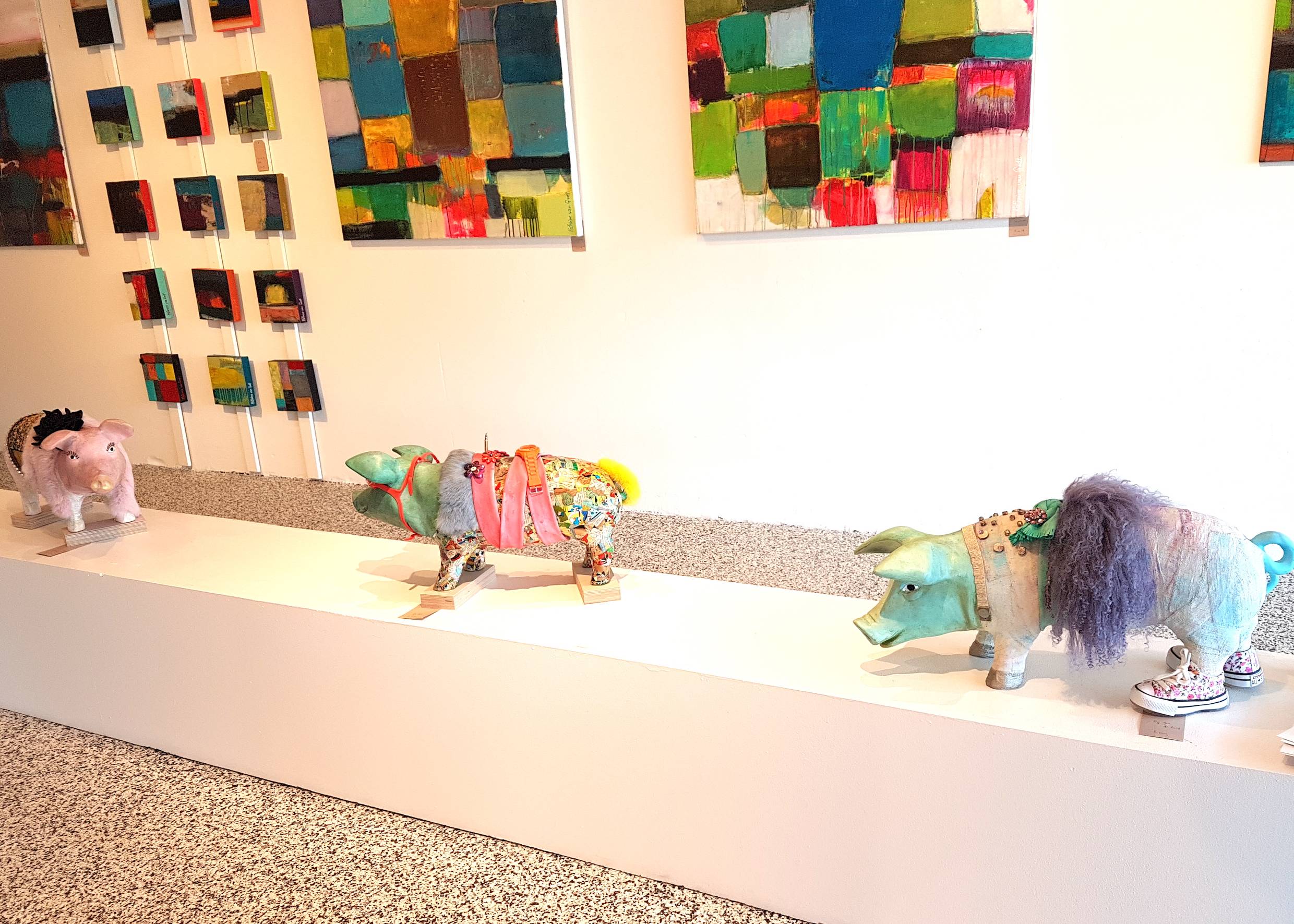 Szene aus einer Galerie, moderne Bilder an der Wand und bunt verzierte Schweine am Boden