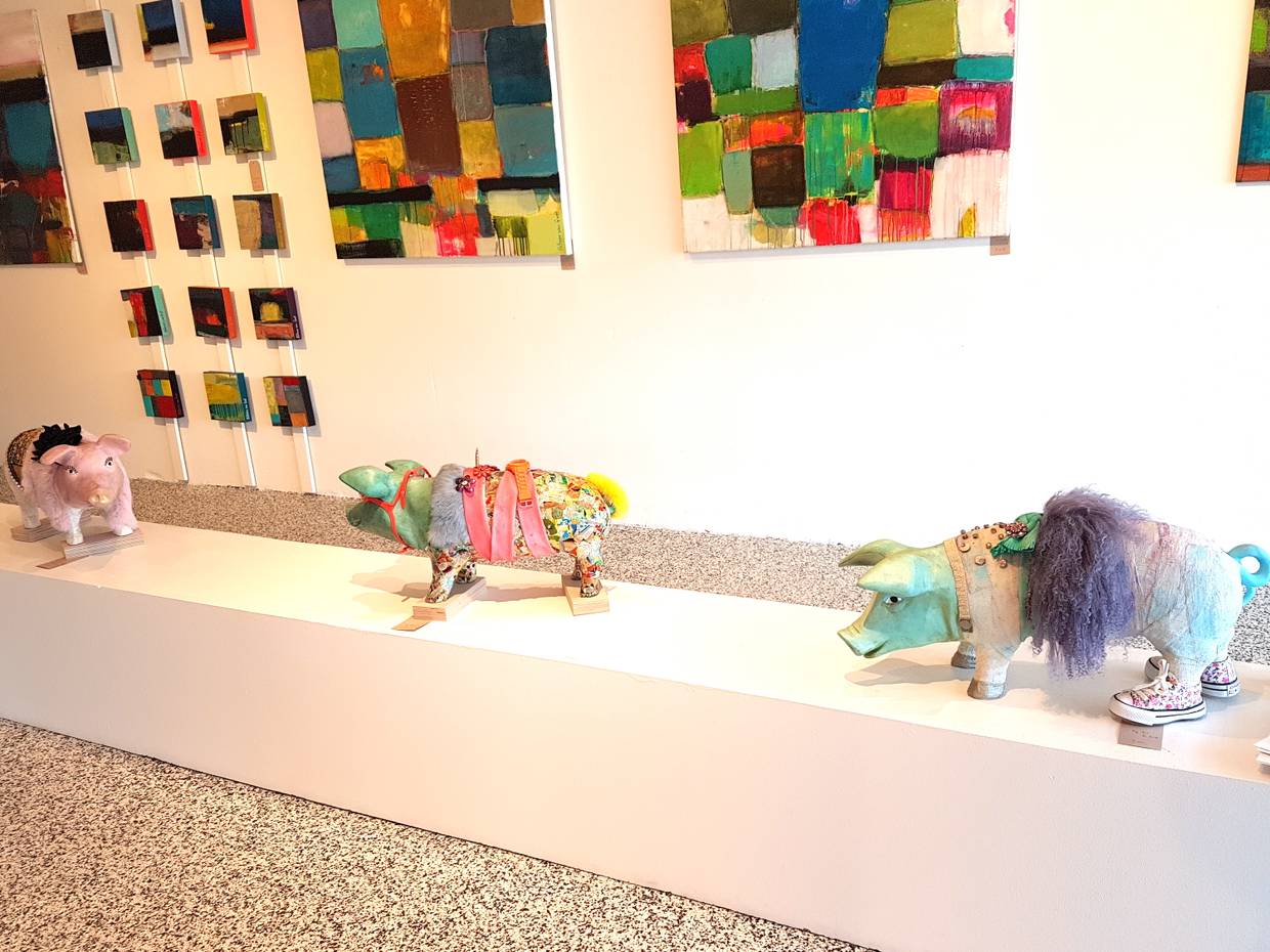 Szene aus einer Galerie, moderne Bilder an der Wand und bunt verzierte Schweine am Boden