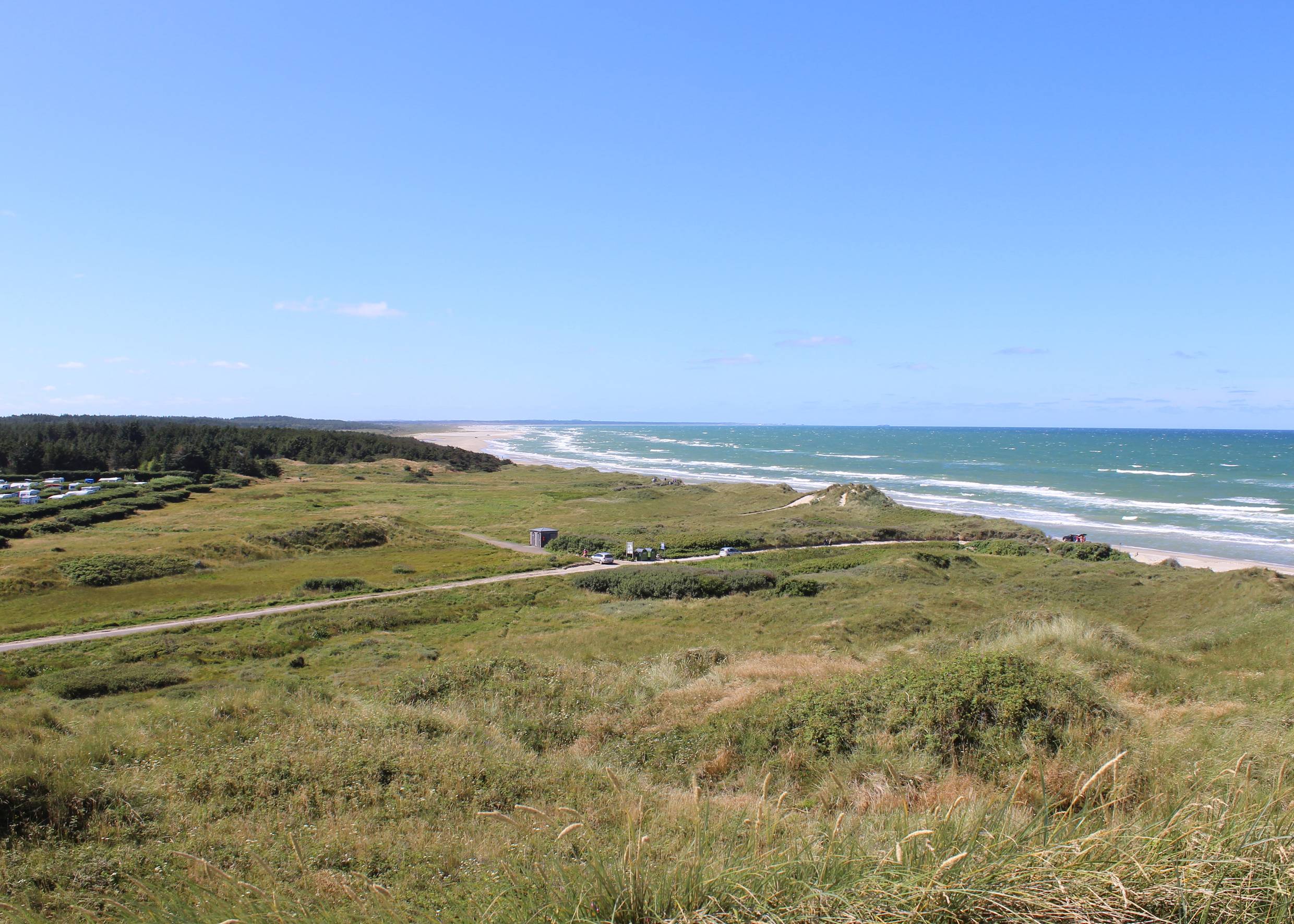 Aussicht über eine langgezogene Bucht, im Hintergrund ein Campingplatz, rechts das Meer