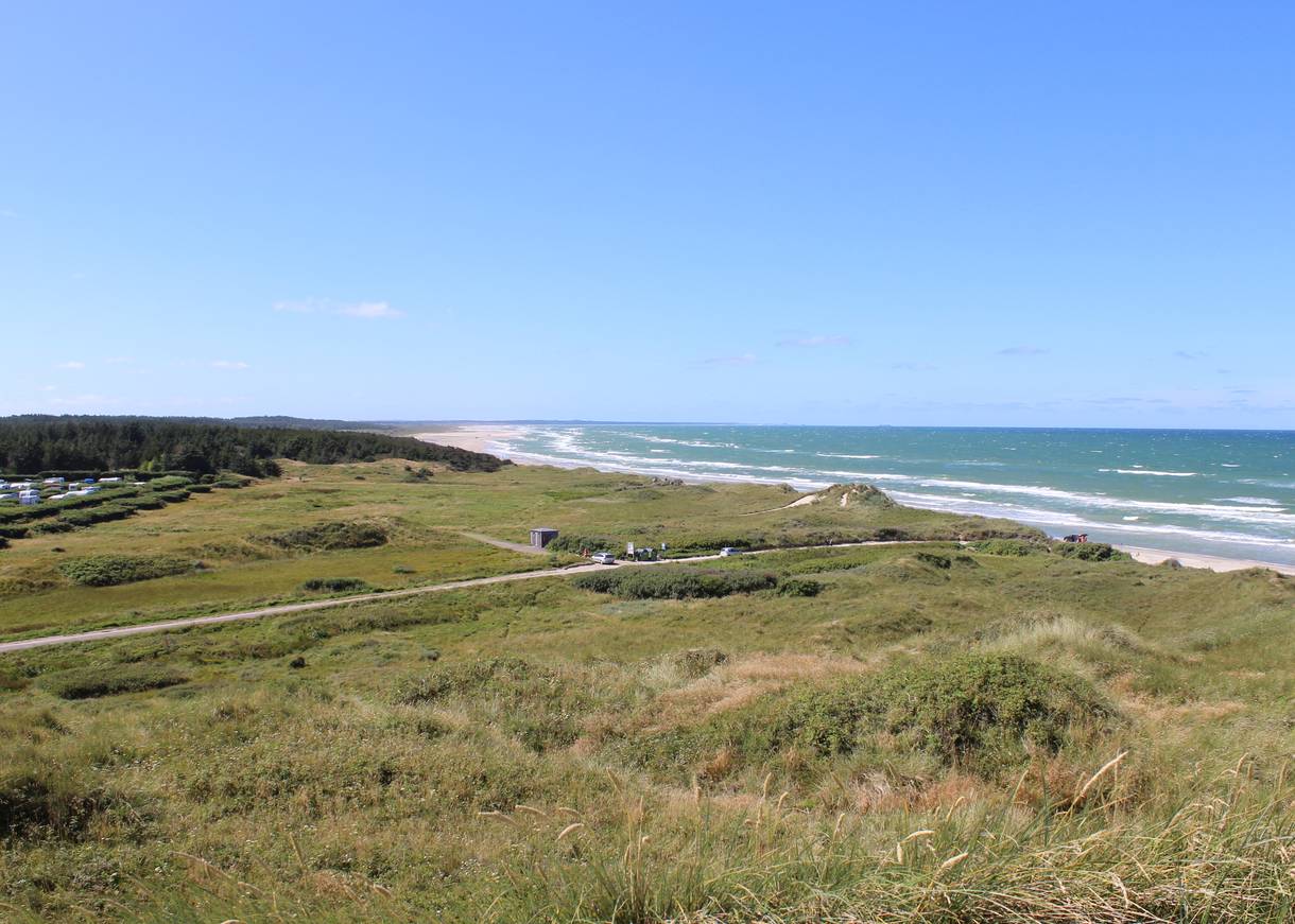 Aussicht über eine langgezogene Bucht, im Hintergrund ein Campingplatz, rechts das Meer