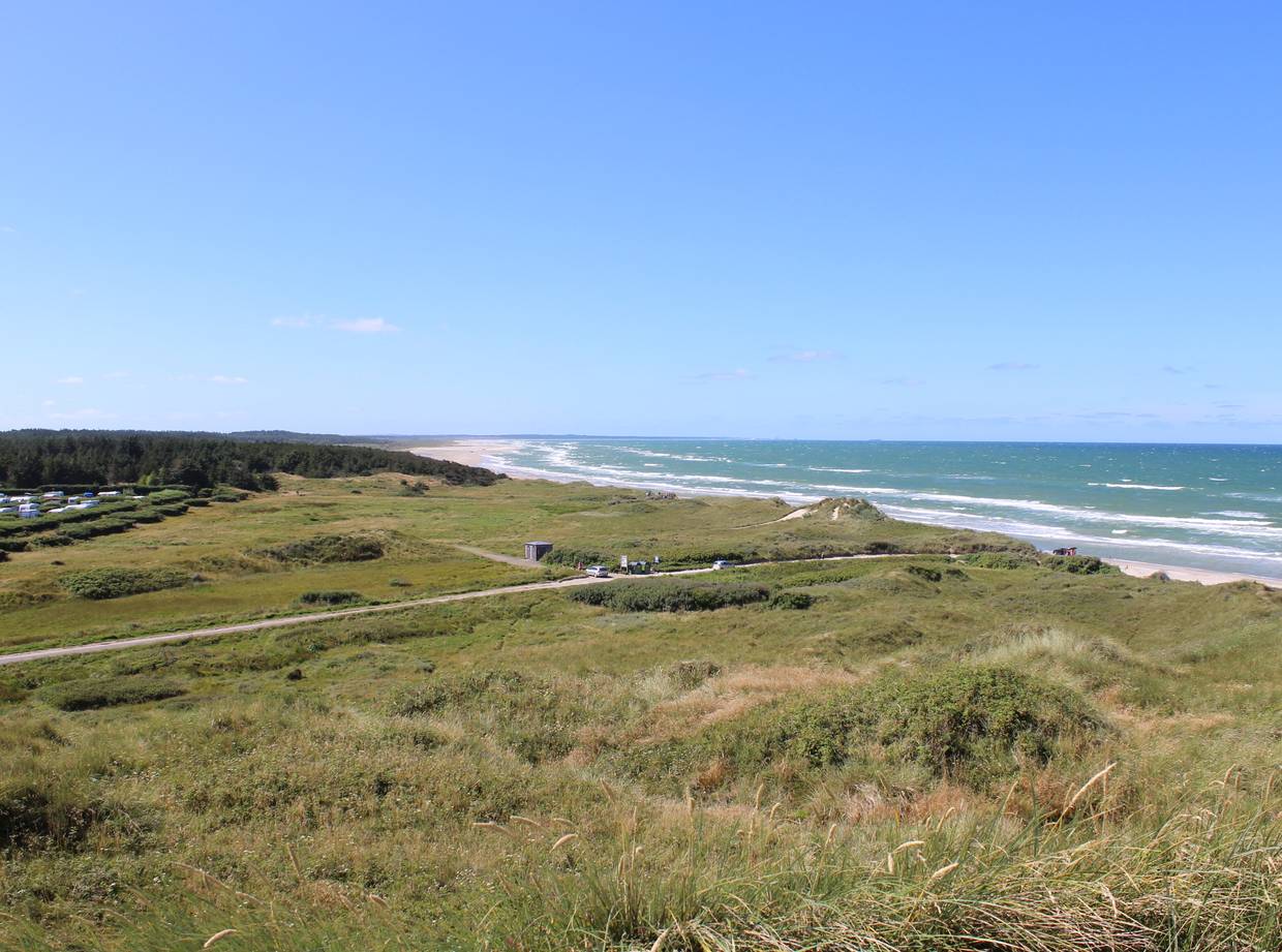 Aussicht über eine langgezogene Bucht, im Hintergrund ein Campingplatz, rechts das Meer