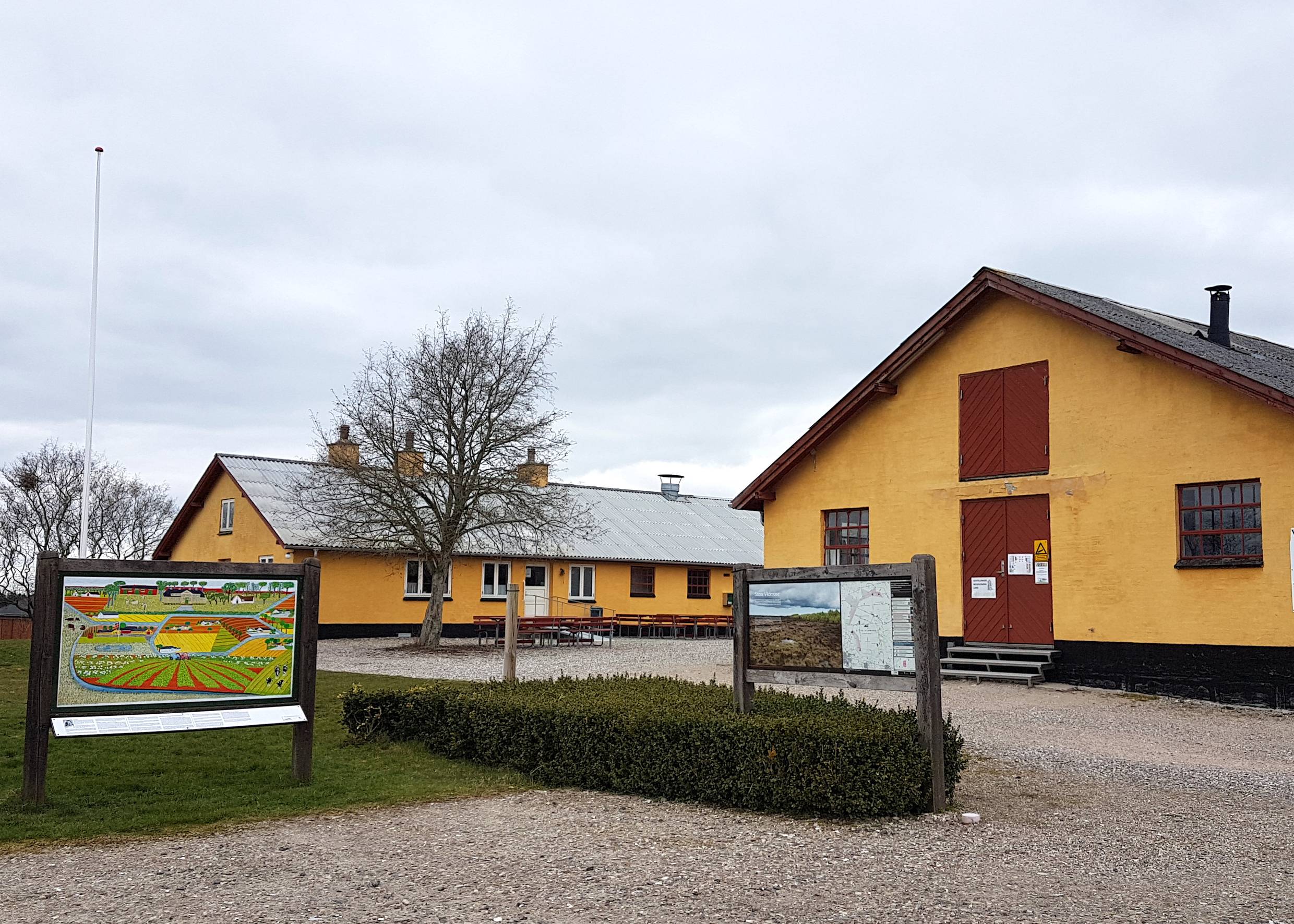 Gelbe Hofanlage mit einem Infoschild vor der Einfahrt