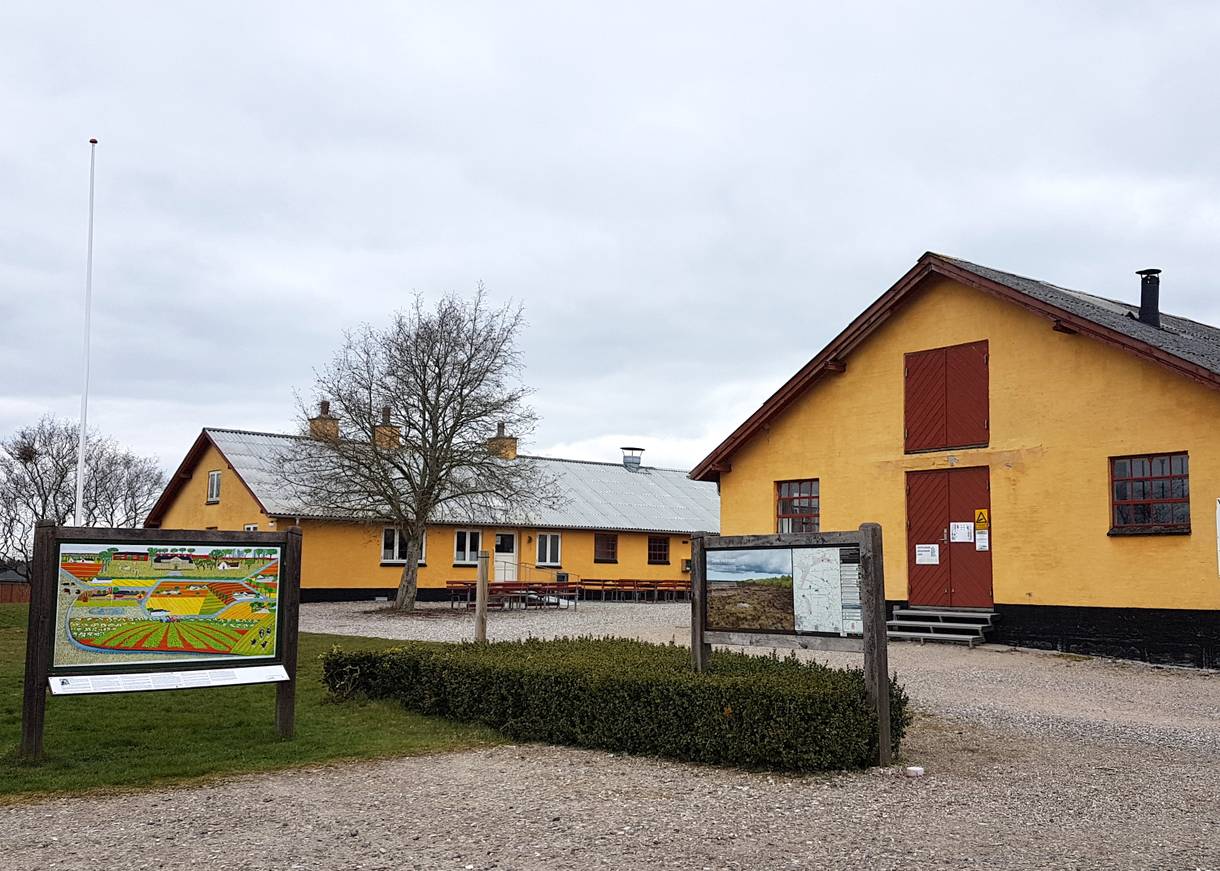 Gelbe Hofanlage mit einem Infoschild vor der Einfahrt