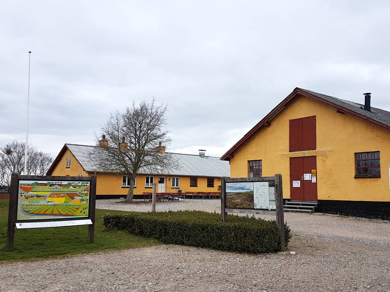Gelbe Hofanlage mit einem Infoschild vor der Einfahrt