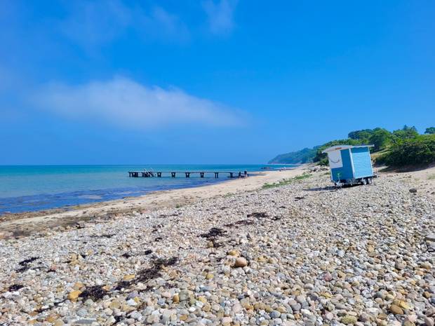 Steinigerstrand mit Badesteg und blauem Bauwagen in Gilleleje, im Hintergrund Steilküste