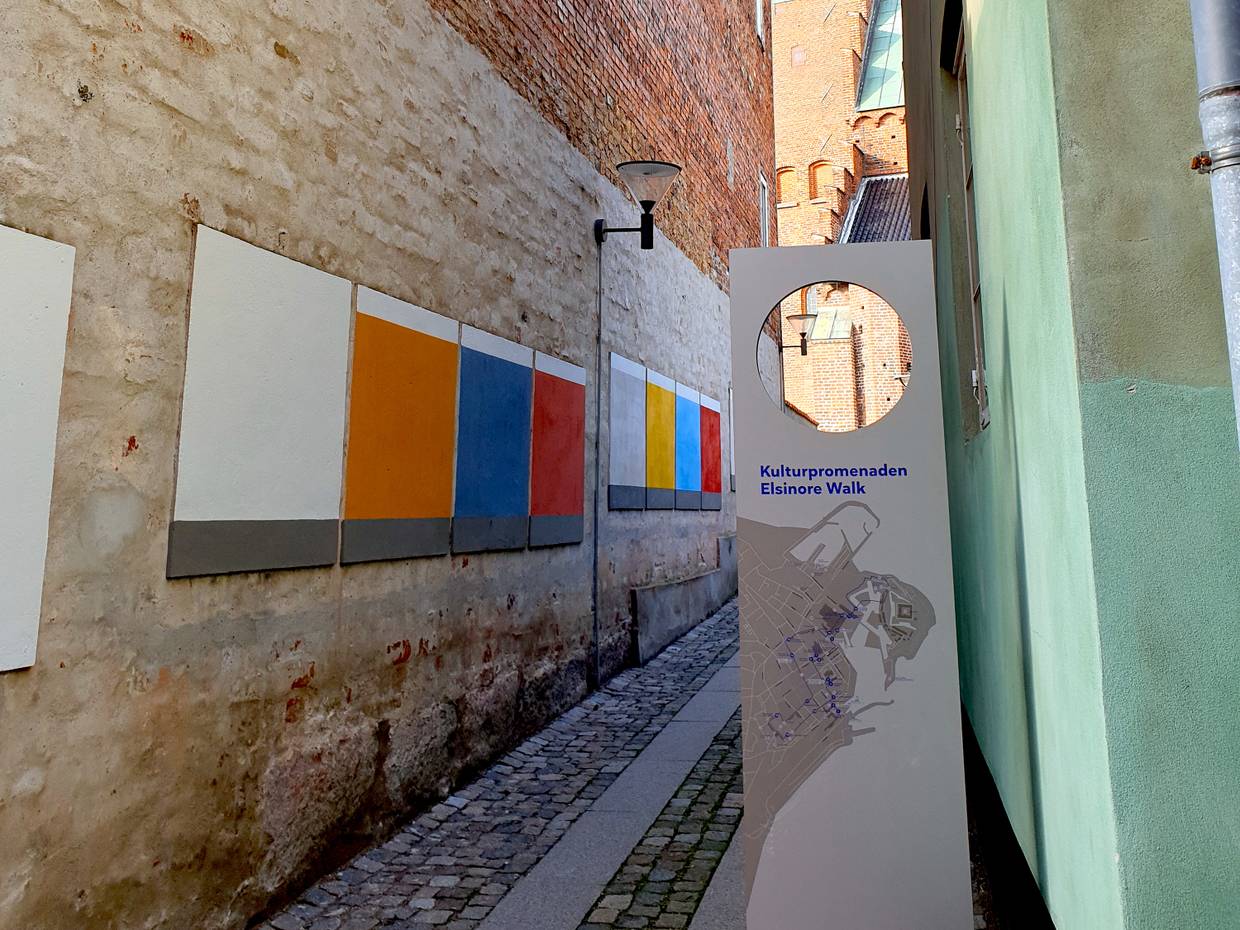 Gasse mit farbflächen an den alten Häusern, davor eine Infotafel zu einem Stadtrundgang