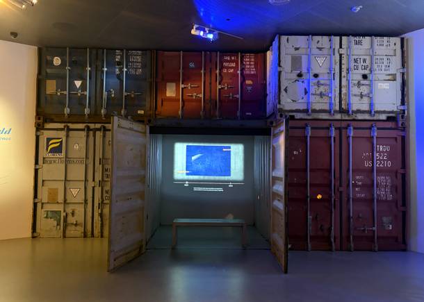 Sechs Container in einem Museumsraum, in einem der Container wird ein Film gezeigt