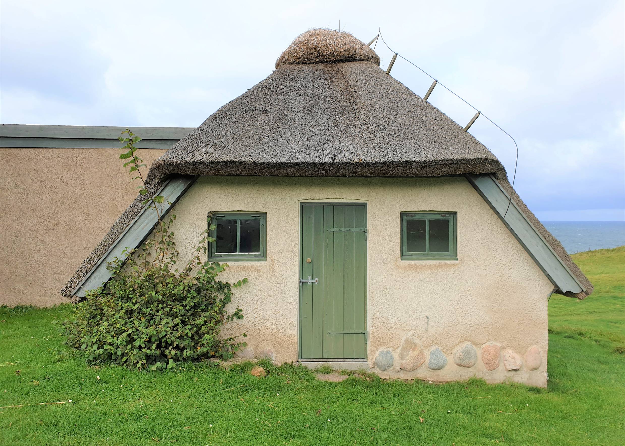Reetdachhaus auf einer hügeligen Wiese am Meer