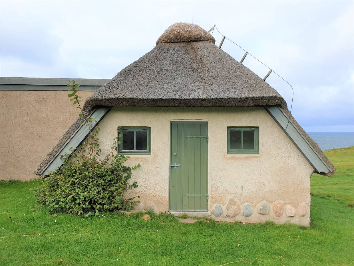 Reetdachhaus auf einer hügeligen Wiese am Meer