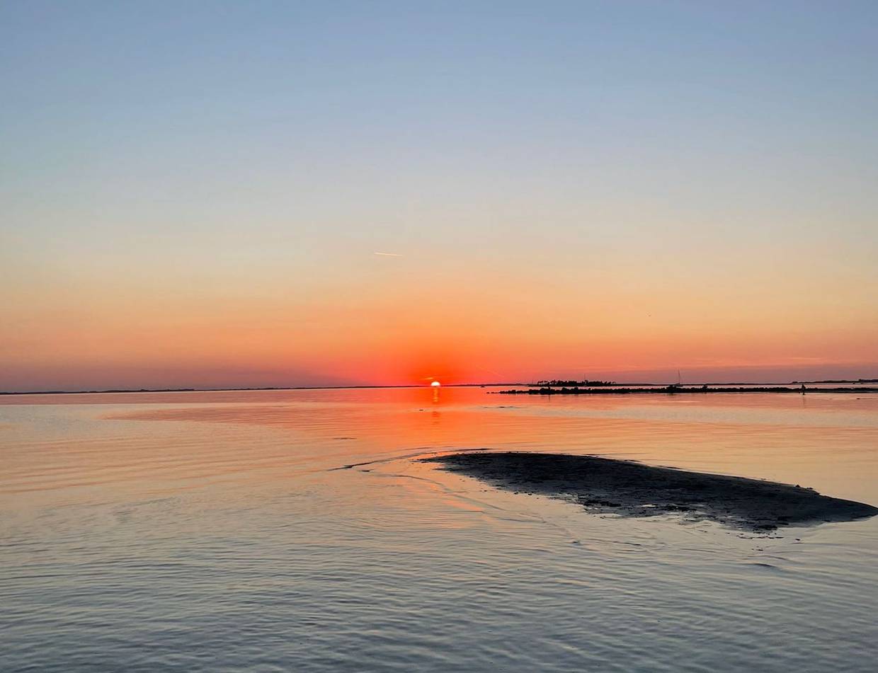 Roter Himmel mit untergehender Sonne über einer Sandbank im flachen Wasser
