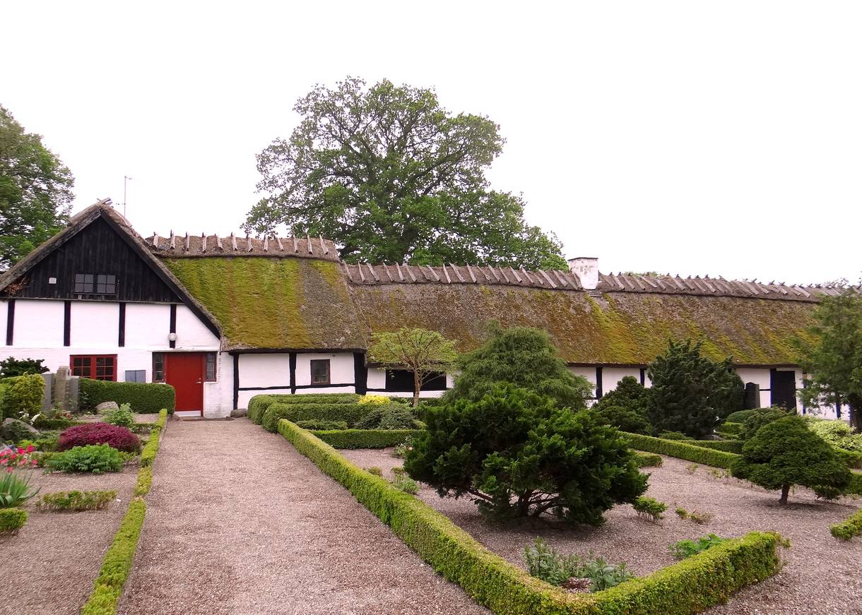 Flaches, weißes Reetdachhaus, davor ein Friedhof
