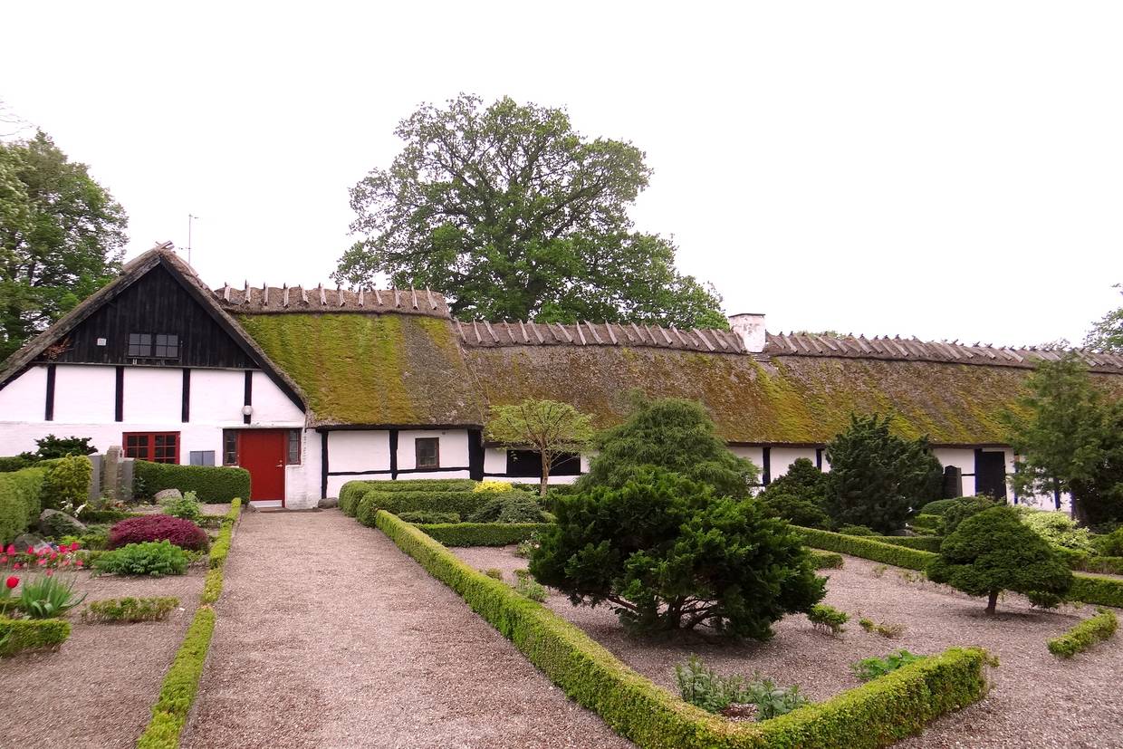 Flaches, weißes Reetdachhaus, davor ein Friedhof