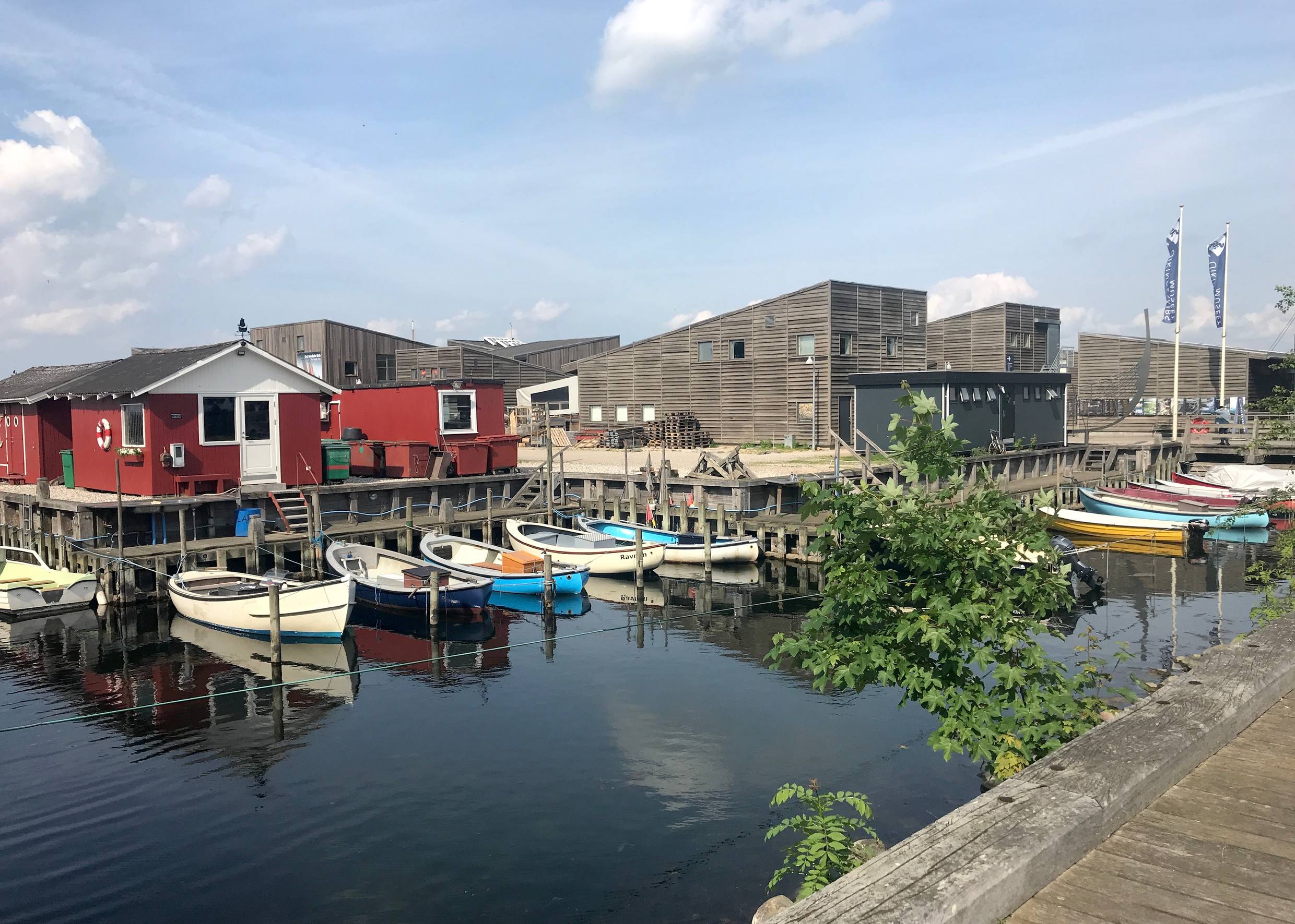 Flaches Holzgebäude am Hafen, davor kleine, bunte Boote