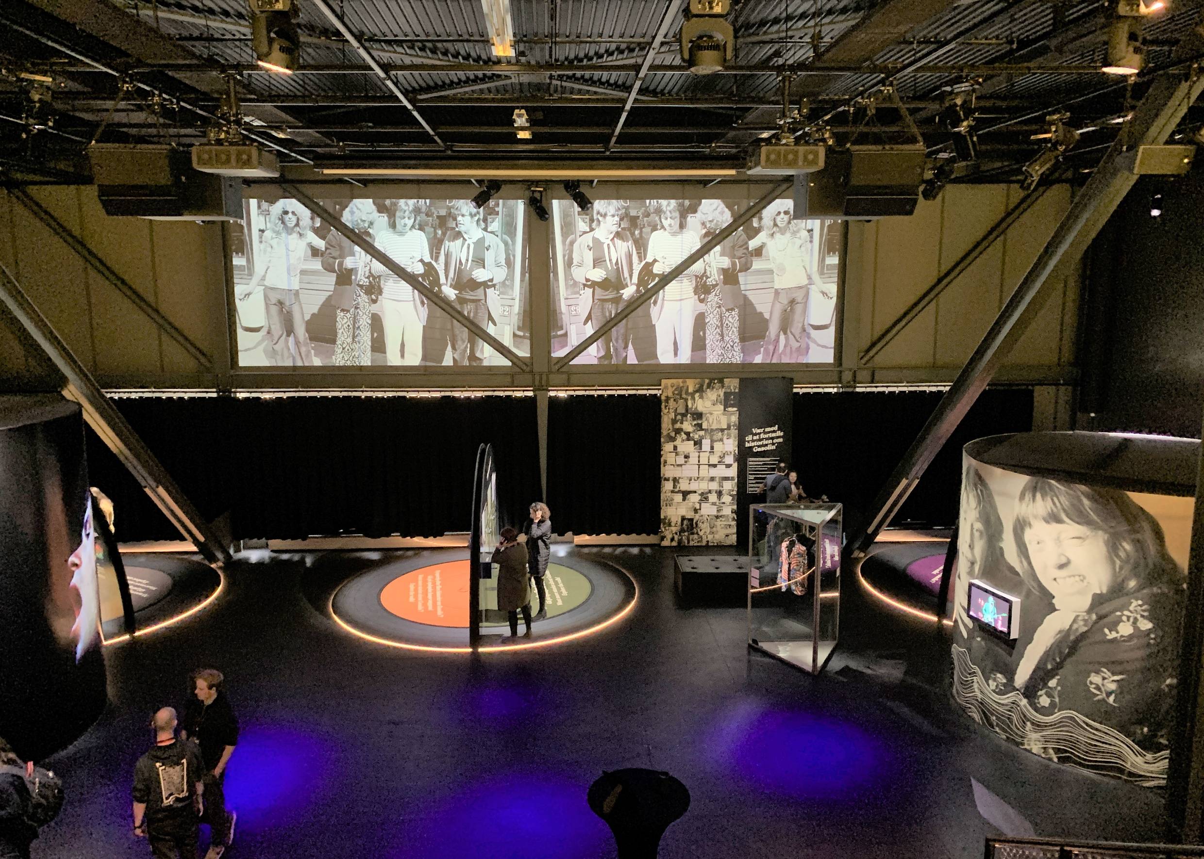 Ausstellungsraum im Popmuseum. Besucher mit Kopfhörern und große Videoleinwände