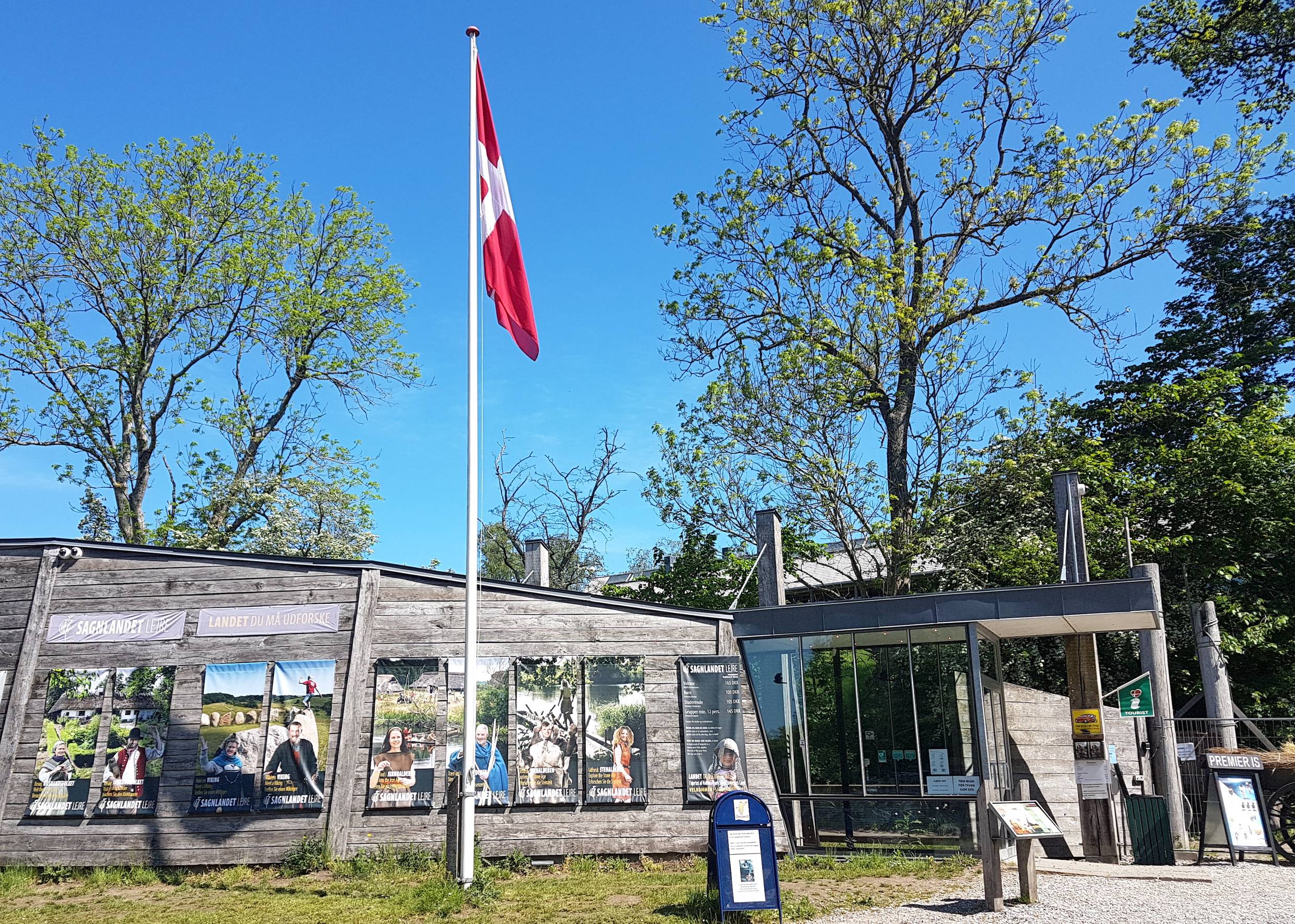 Eingangsgebäude zum Freiluftmuseum, Plakate an der Hauswand, davor ein Fahnenmast
