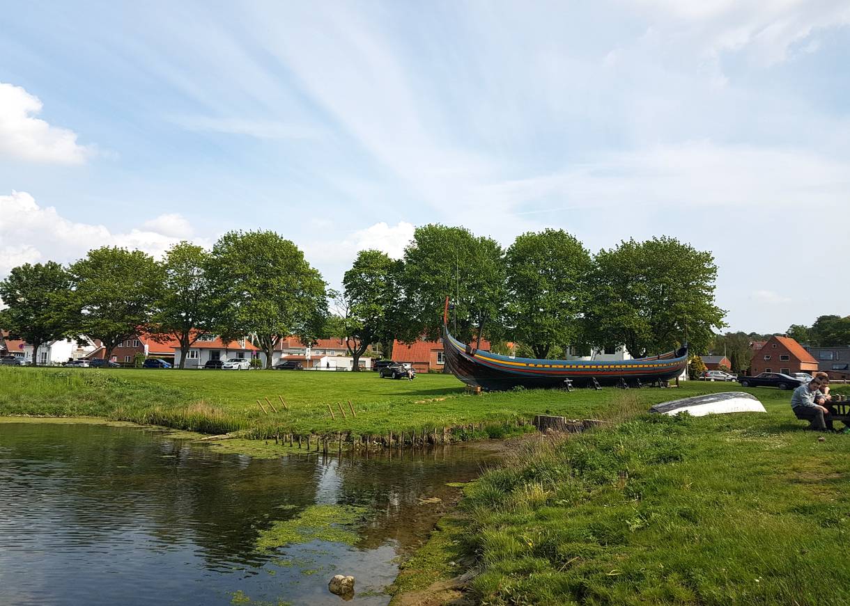 Farbiges Holzboot auf einer Wiese, dahinter Wohnhäuser