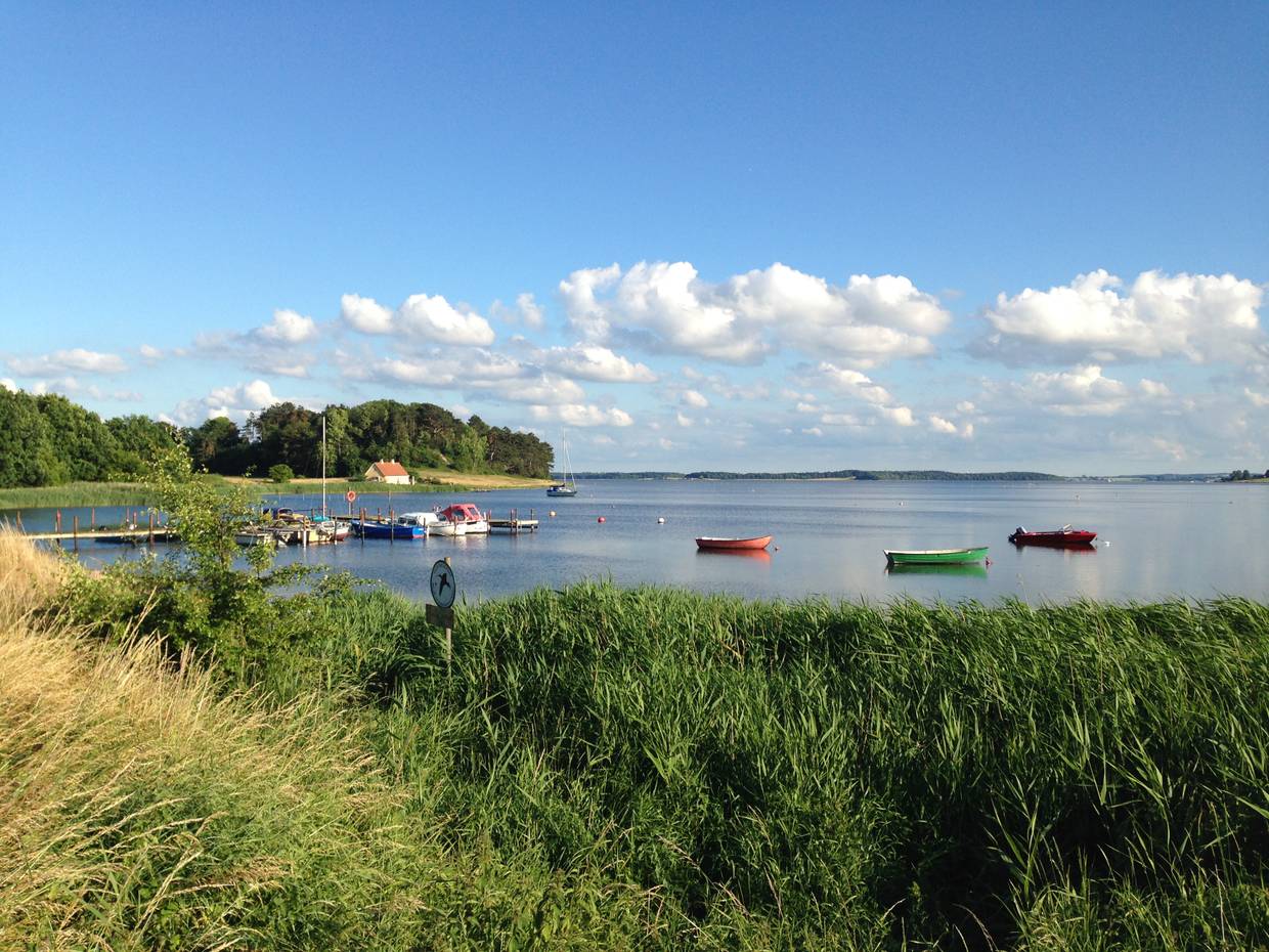 Bootssteg in einer grün umrandeten Bucht, im Wasser bunte Boote unter blauem Himmel