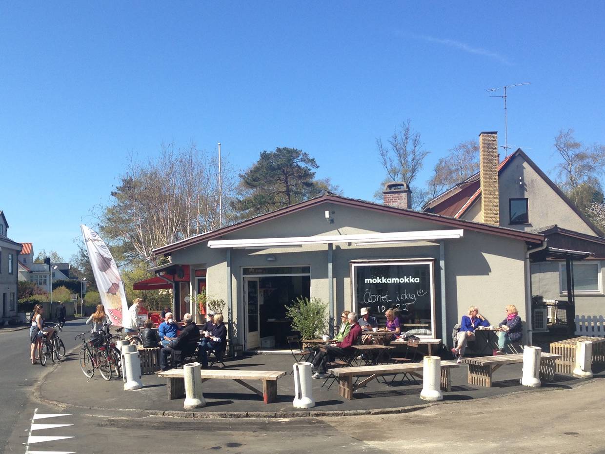 Café an einer Straßenecke, vor der Tür viele Gäste 