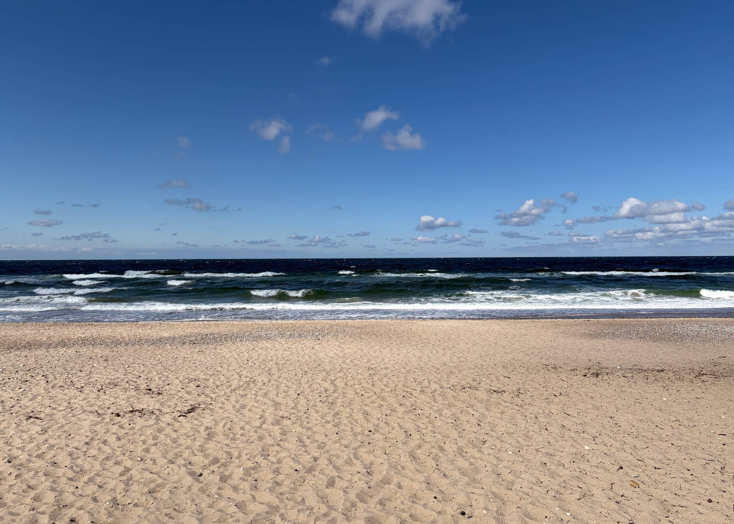Breiter Sandstrand, in der Ferne ein Spaziergänger