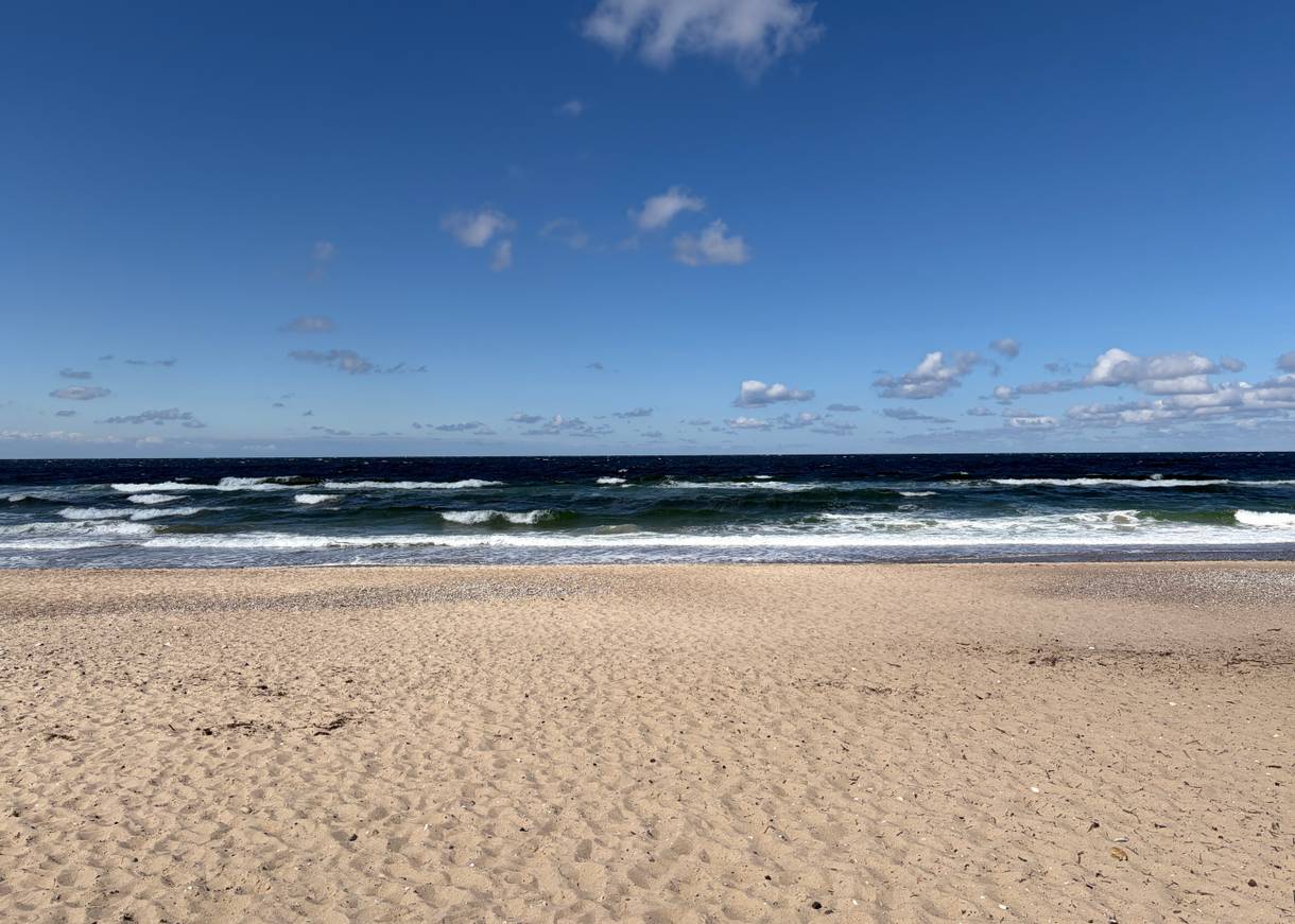 Breiter Sandstrand, in der Ferne ein Spaziergänger