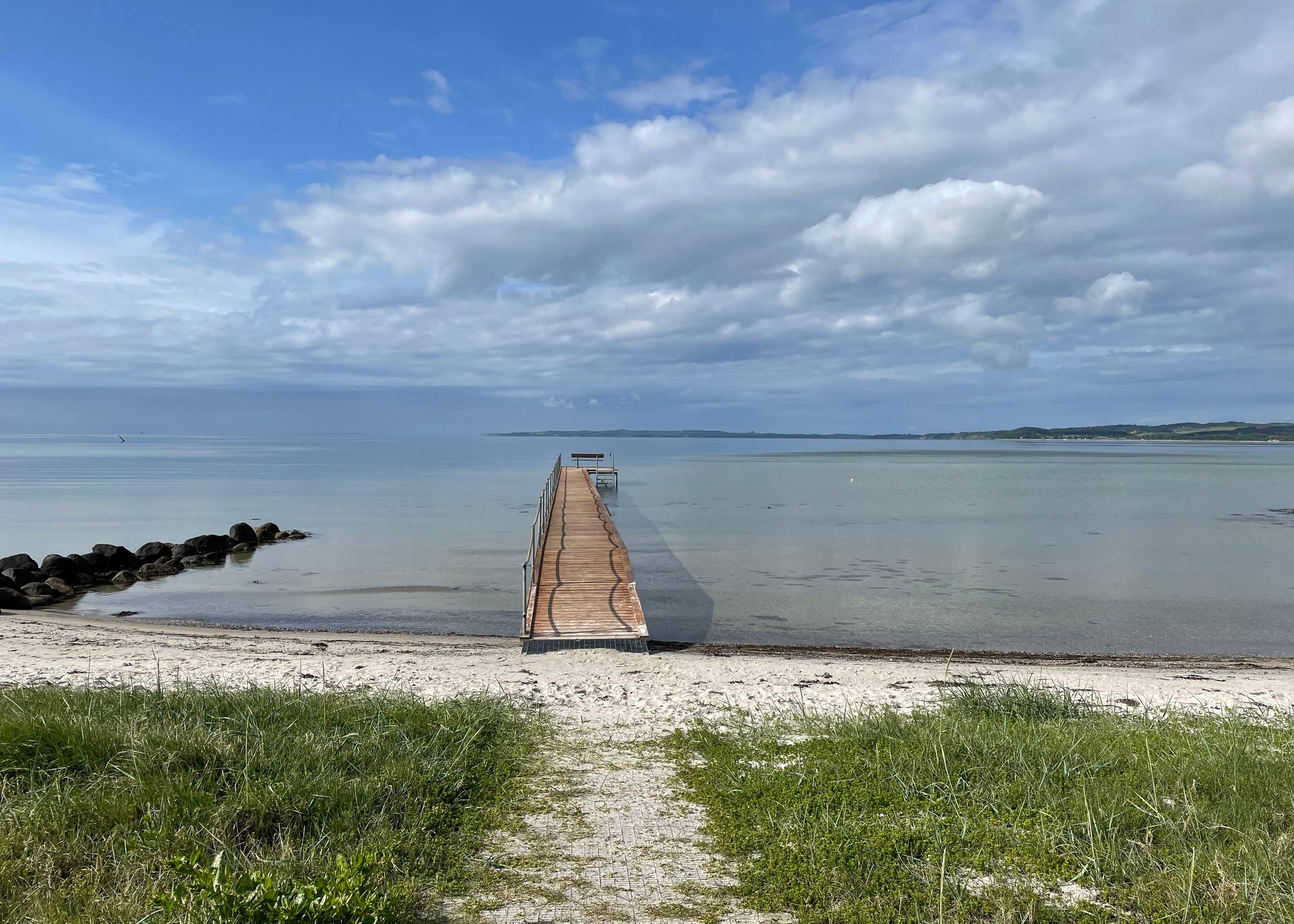 Badesteg an einer flachen Bucht bei Ebeltotf mit grüner Küstenionie am Horizont