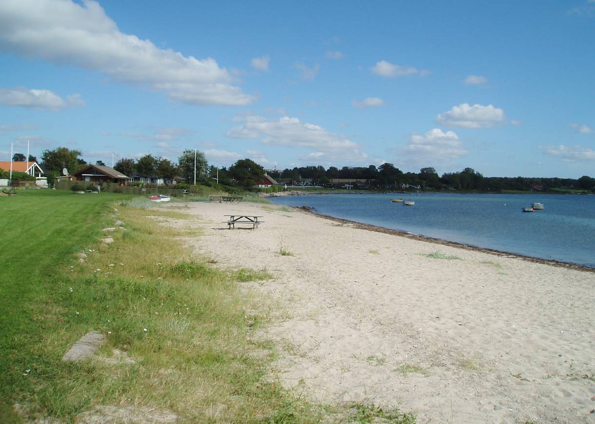 Schmaler Sandstrand, im Hintergrund Ferienhäuser mit Meerblick